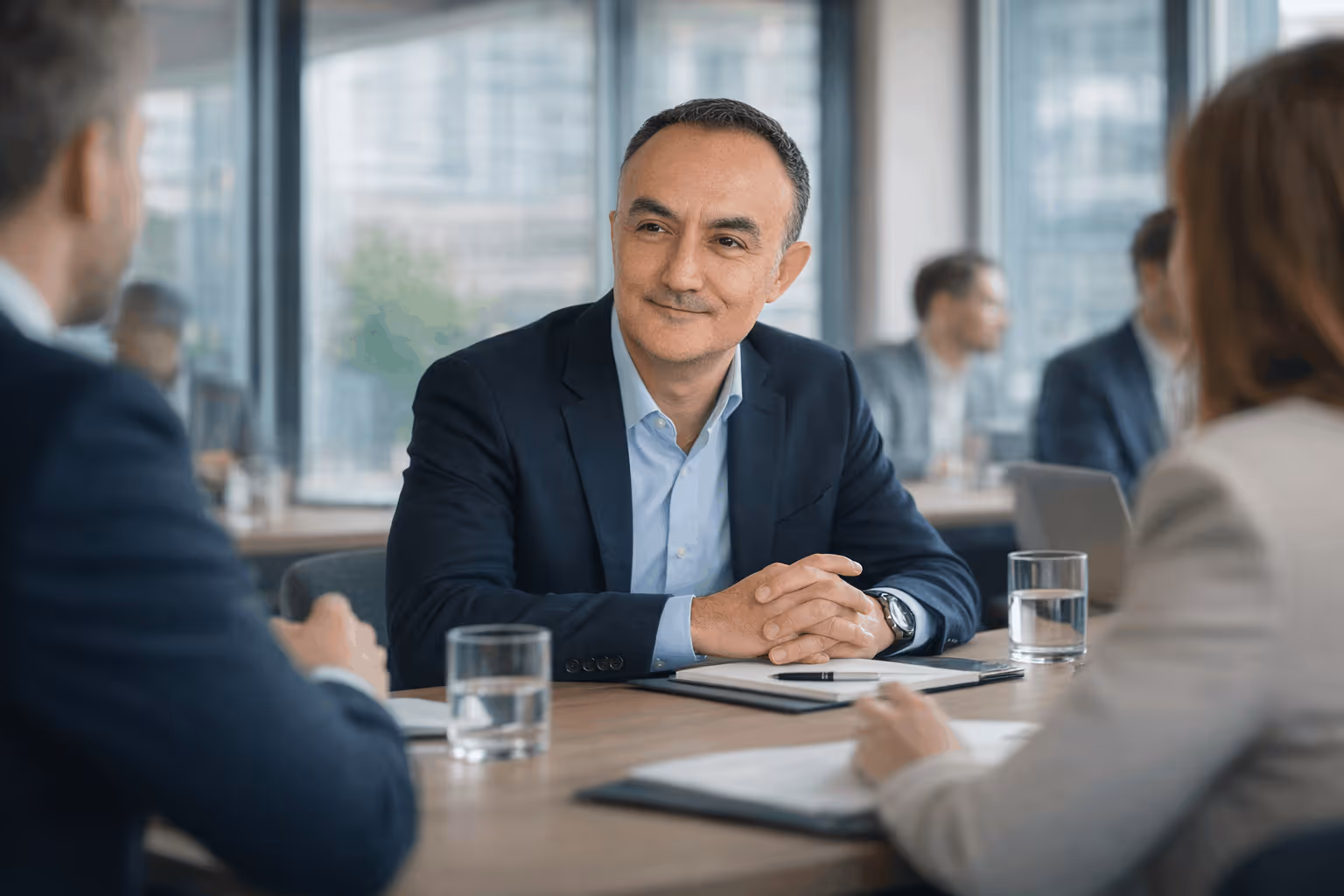 Fractional executive in a suit smiling and sitting at a conference table with two colleagues in a modern office.