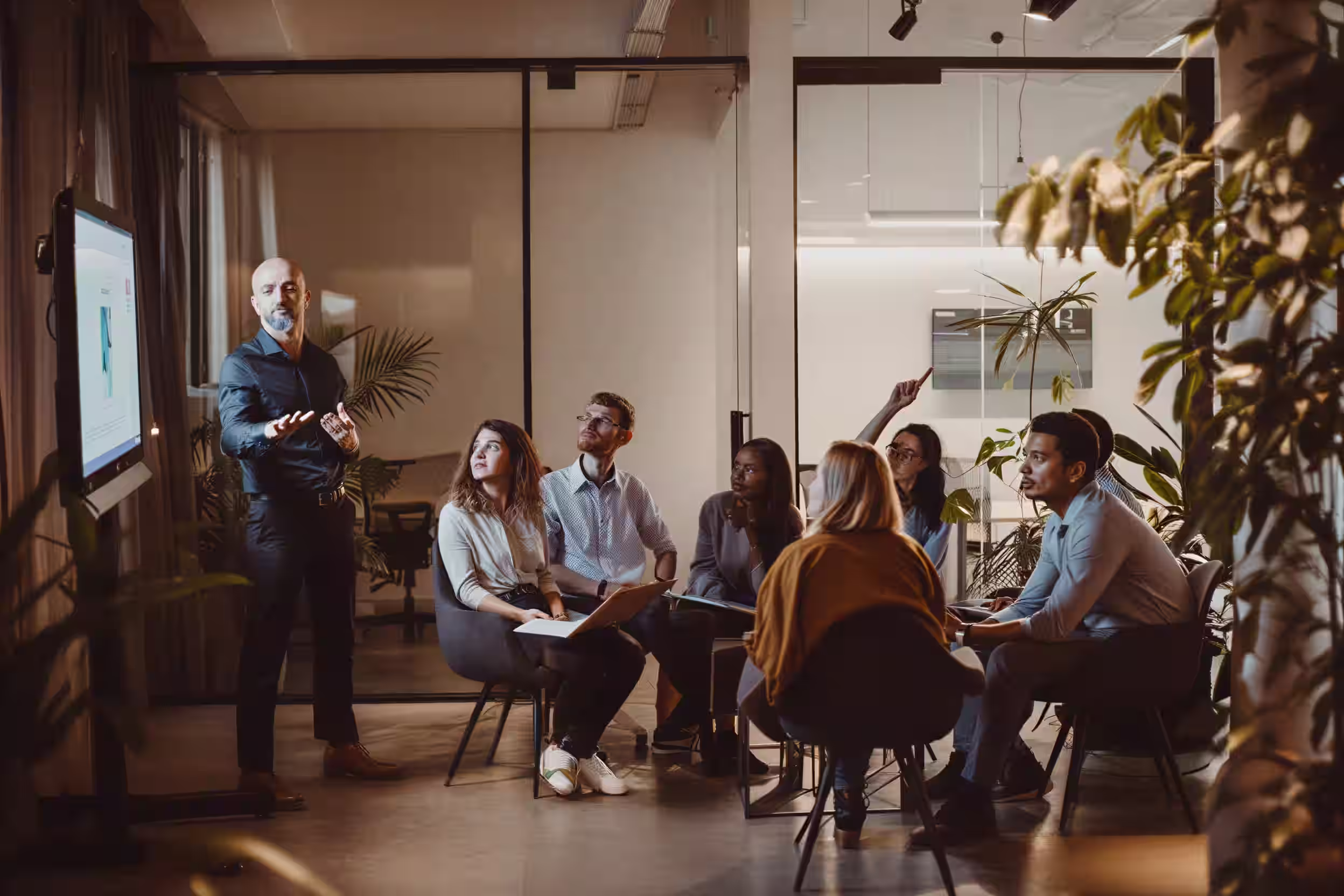 Fractional executive giving a presentation on cyber security to a diverse group of six seated colleagues in a modern office meeting room with glass walls and plants.